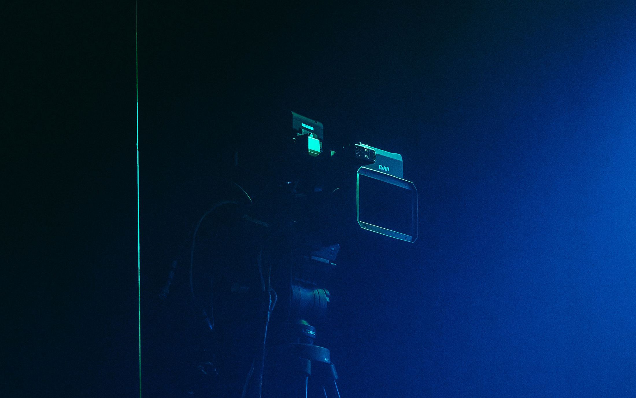 A cinema camera on a tripod in blue light